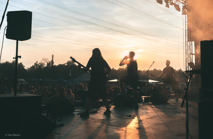 Photo of the band on an open air stage appearing as silhouettes as the sun is shining down on them from off stage