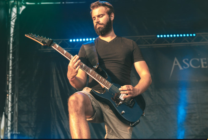 Photo of Markus playing his guitar on an open air stage.